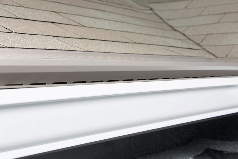 A white vented aluminum soffit installed beneath the edge of a tan shingled roof.