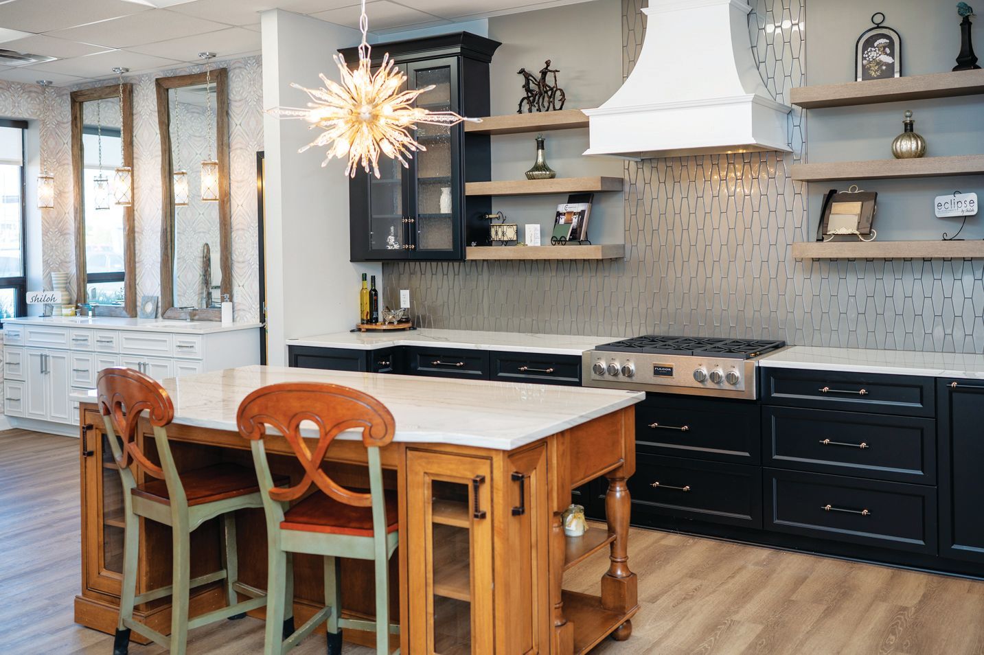 A modern kitchen featuring a wood-toned island with two chairs, black cabinetry, open shelving, and a white vent hood.