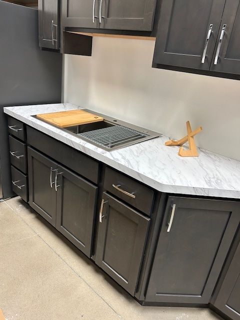 Dark gray kitchen cabinets with silver handles and a white marble-patterned countertop featuring a built-in metal sink.