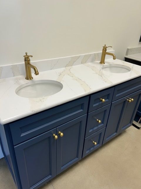 Double vanity with navy blue cabinets, white marble-patterned countertop, and two gold-toned faucets.