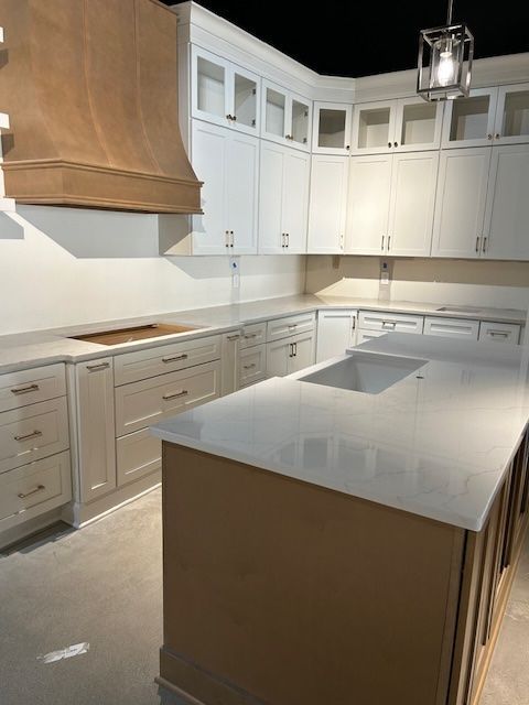 A bright kitchen under construction featuring white cabinets, a wooden range hood, and a large island with a quartz top.