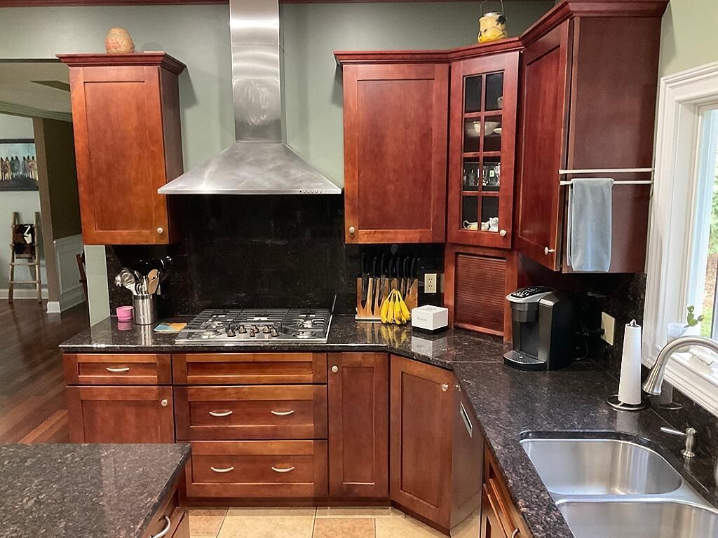 A kitchen with cherry wood cabinets, black granite countertops, a stainless steel range hood, and a dual-basin sink.