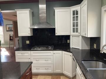 A kitchen with white cabinets, a black countertop, a stainless steel range hood, and dark grey walls.