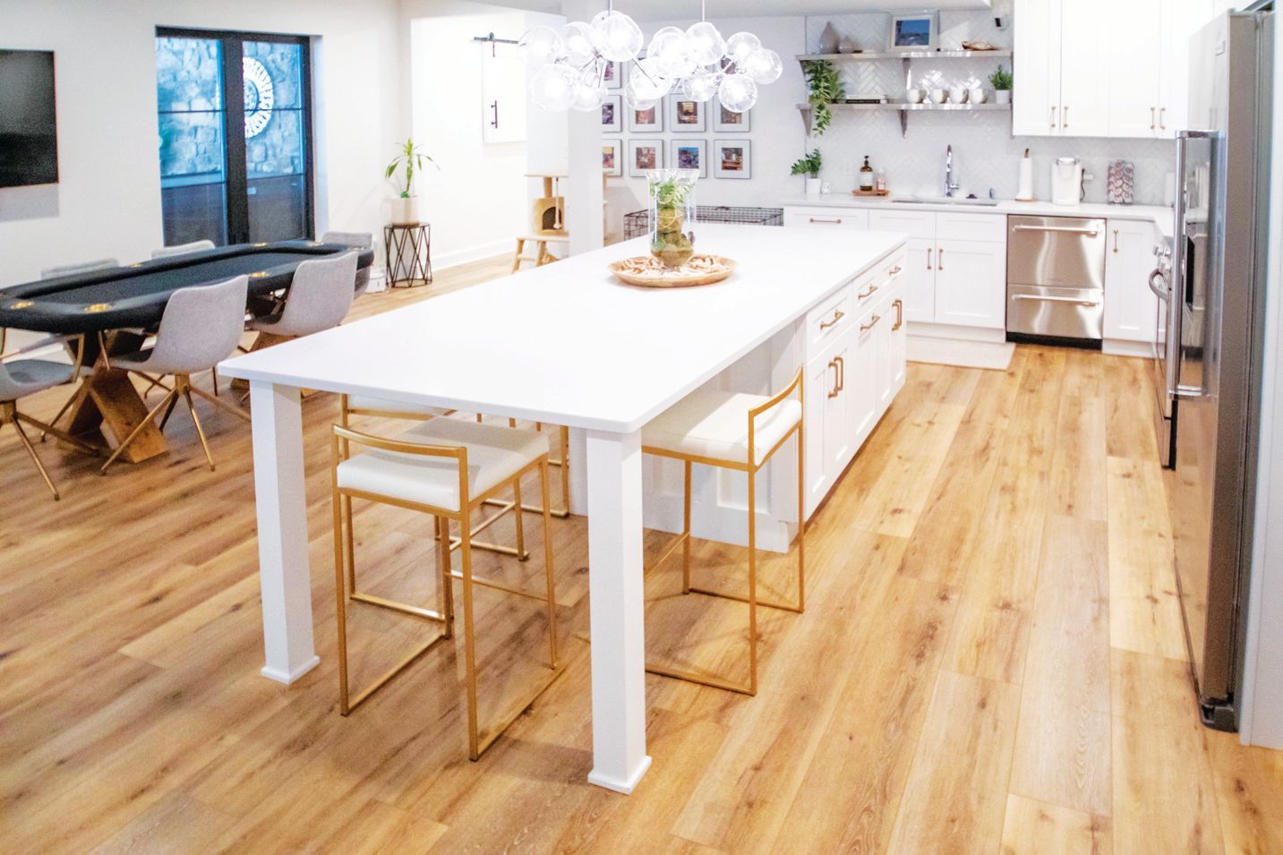 A modern, open-concept kitchen featuring a large white island with gold-framed bar stools and hardwood floors.