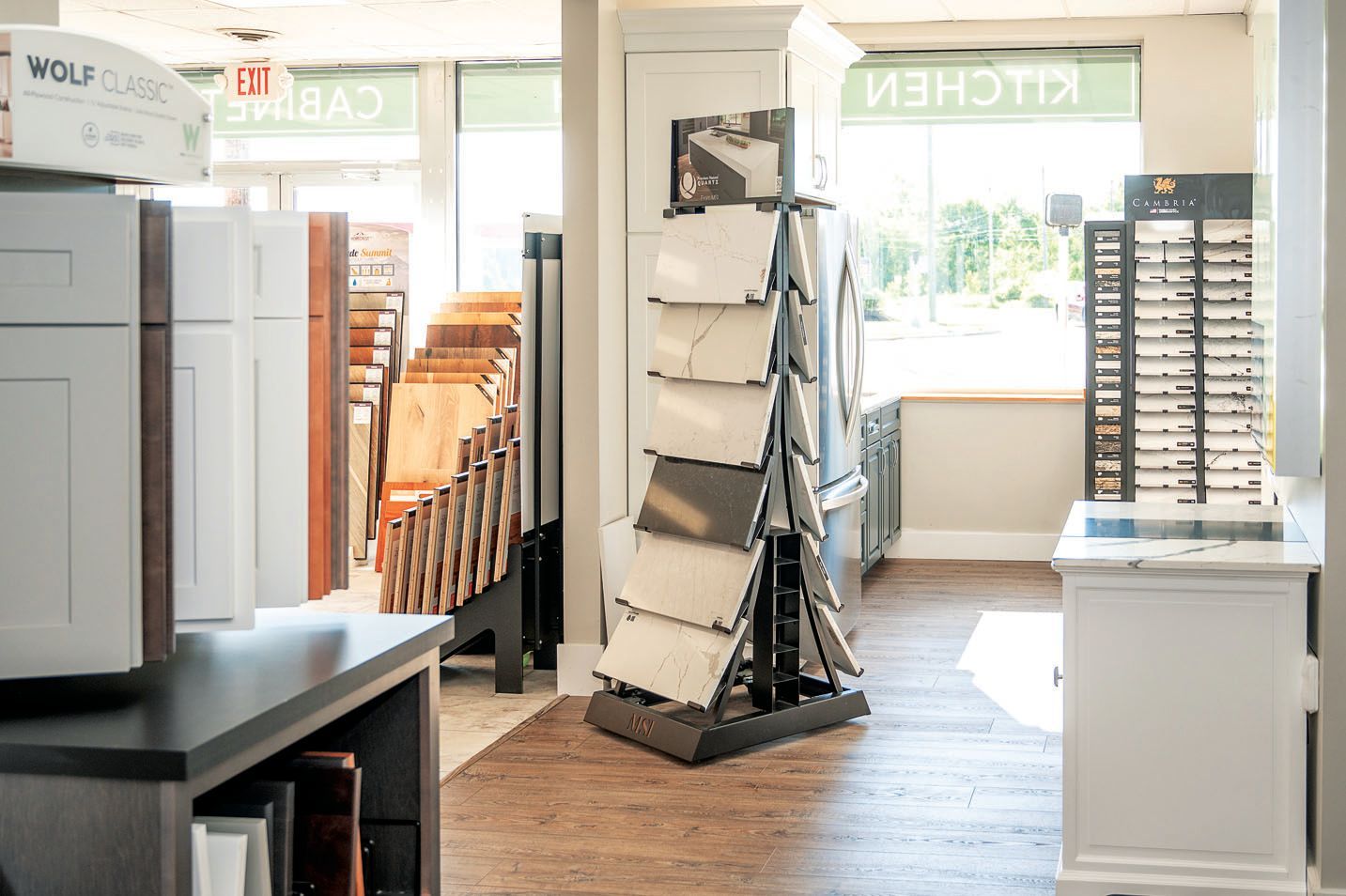 A kitchen showroom interior featuring displays of cabinet doors, flooring samples, and countertop swatches.