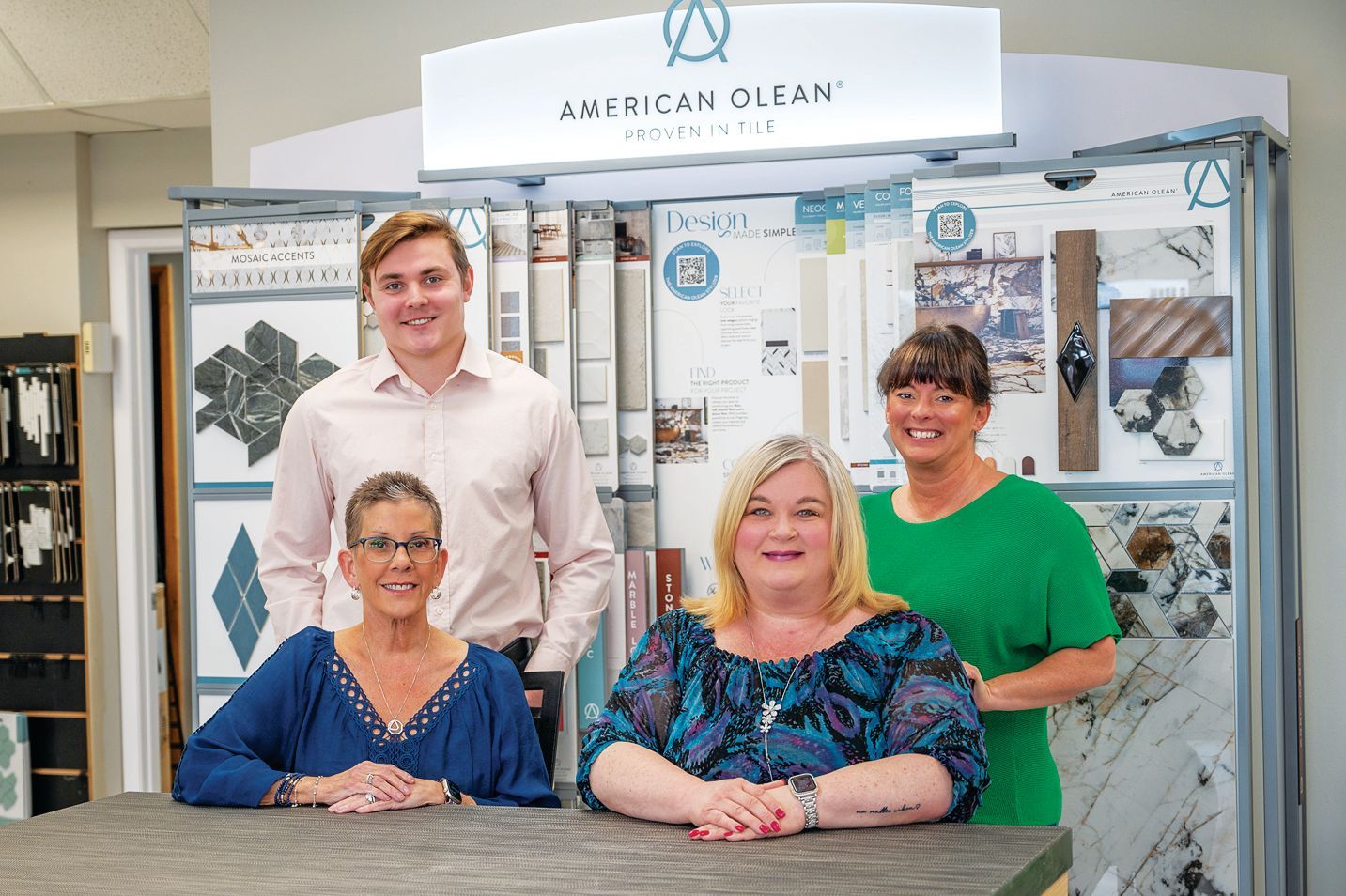 Four people standing together in a store showroom in front of American Olean tile displays.