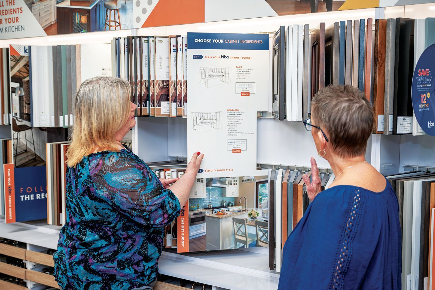 Two people stand in a store display aisle, reviewing a product information sign hanging among rows of material samples.