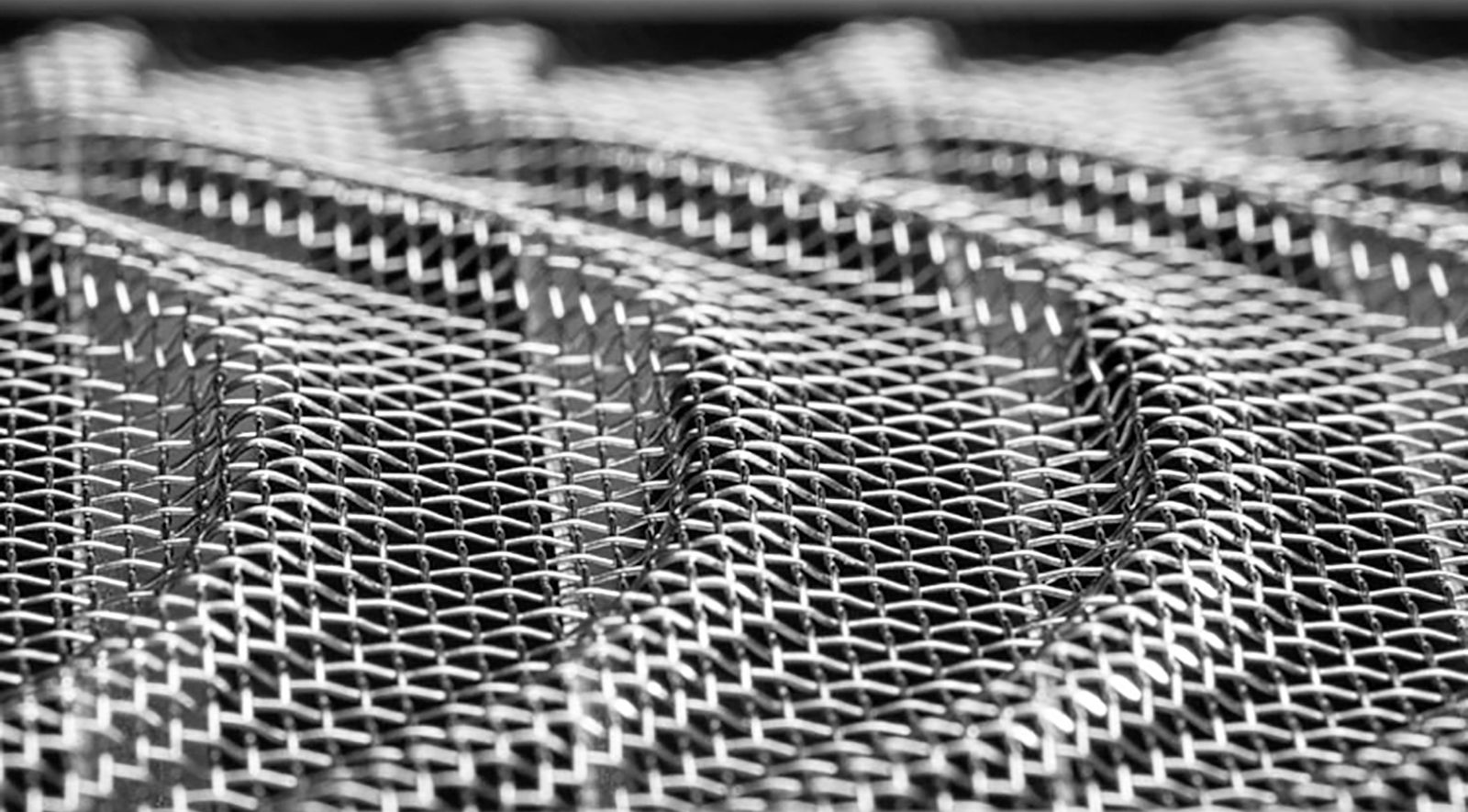 A close-up, black and white abstract pattern of repeating, wavy ridges made of a fine, metallic wire mesh grid.