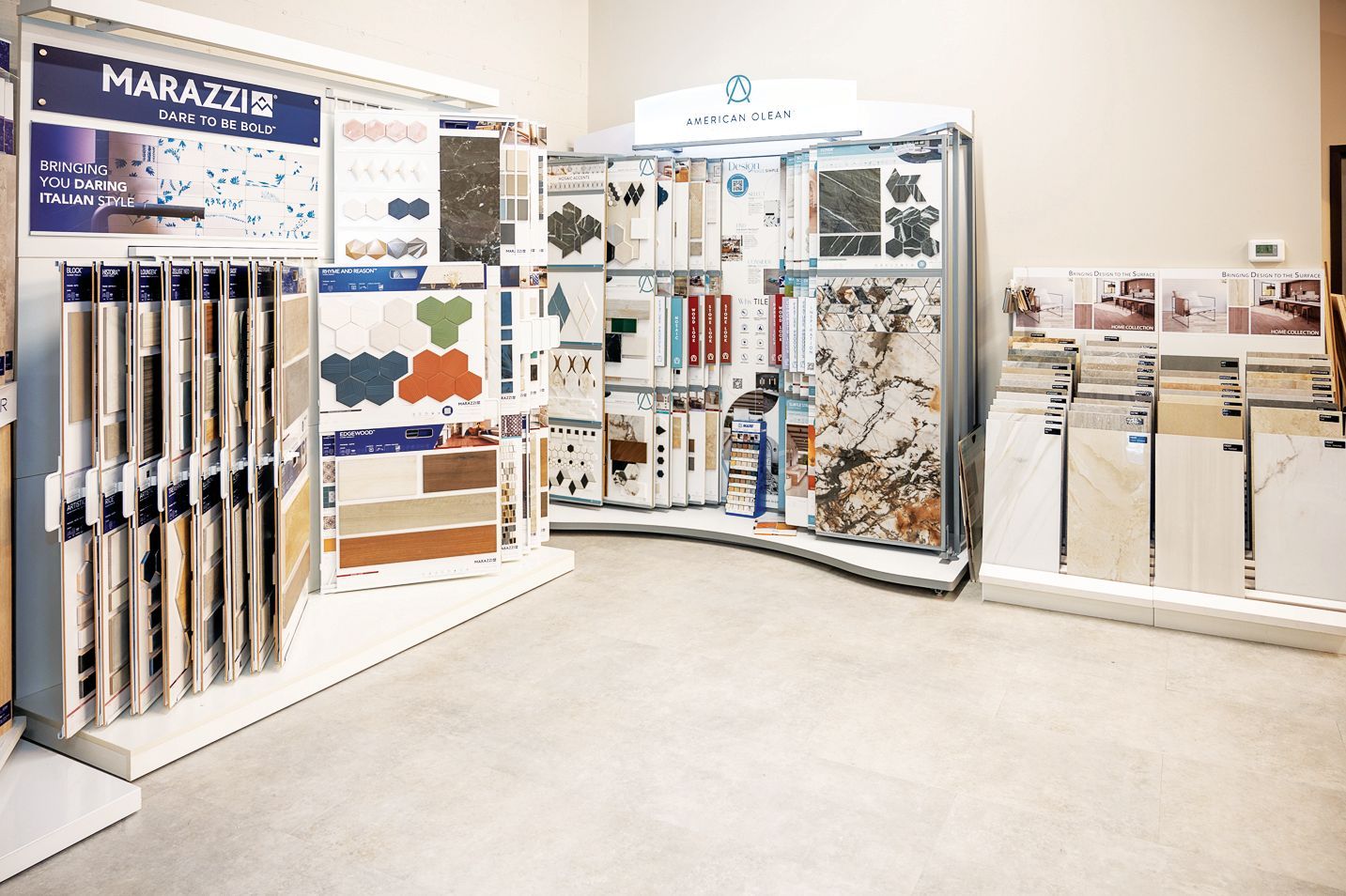 A tile showroom display featuring various sample boards, tile patterns, and stone textures organized on shelving units.