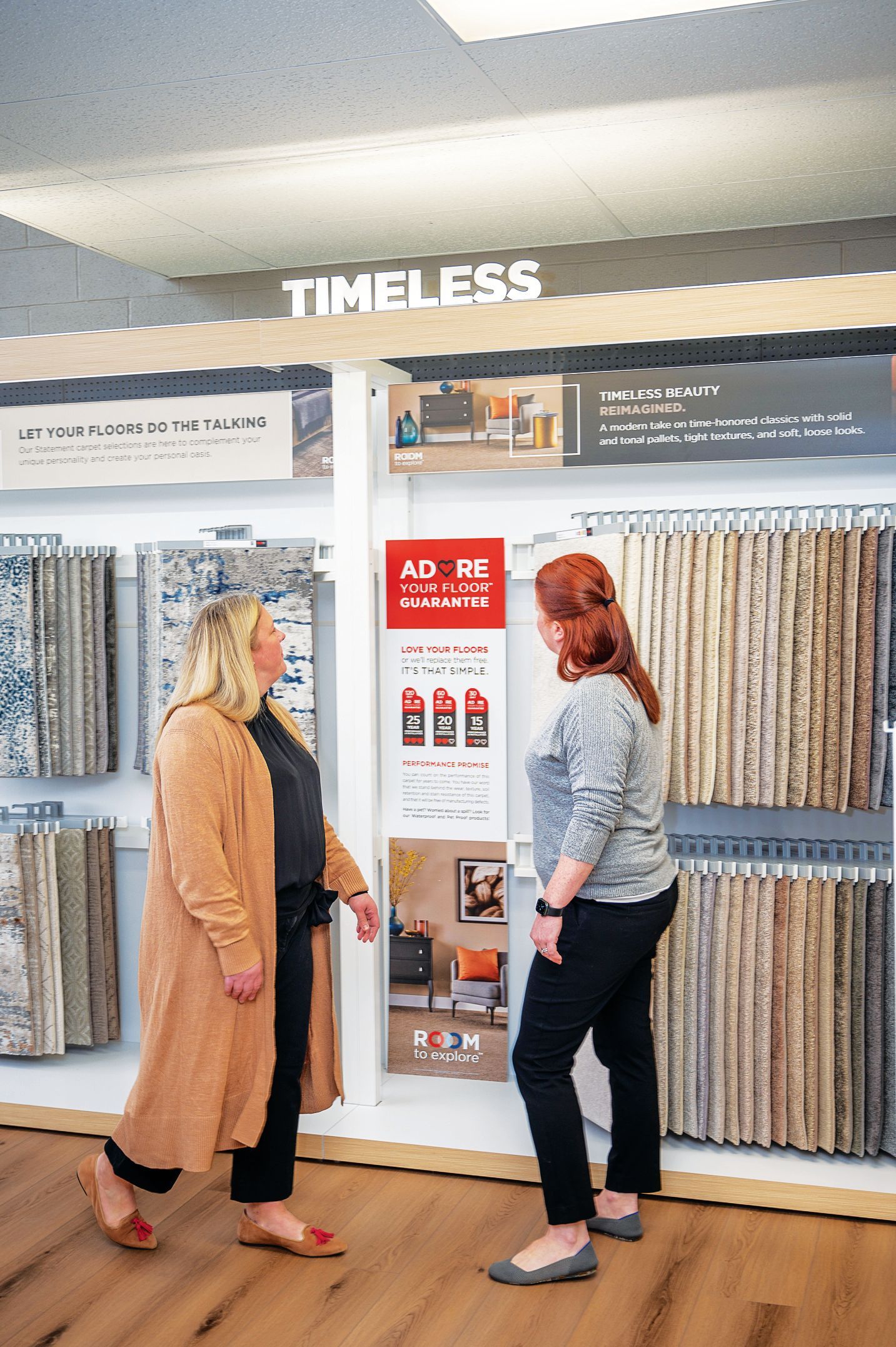 Two people stand in a showroom, reviewing fabric and material samples displayed on wall racks under a Timeless sign.