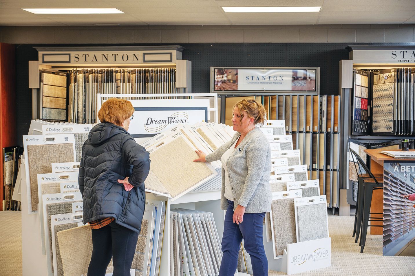 Two people in a carpet store looking at fabric samples displayed on a rack.
