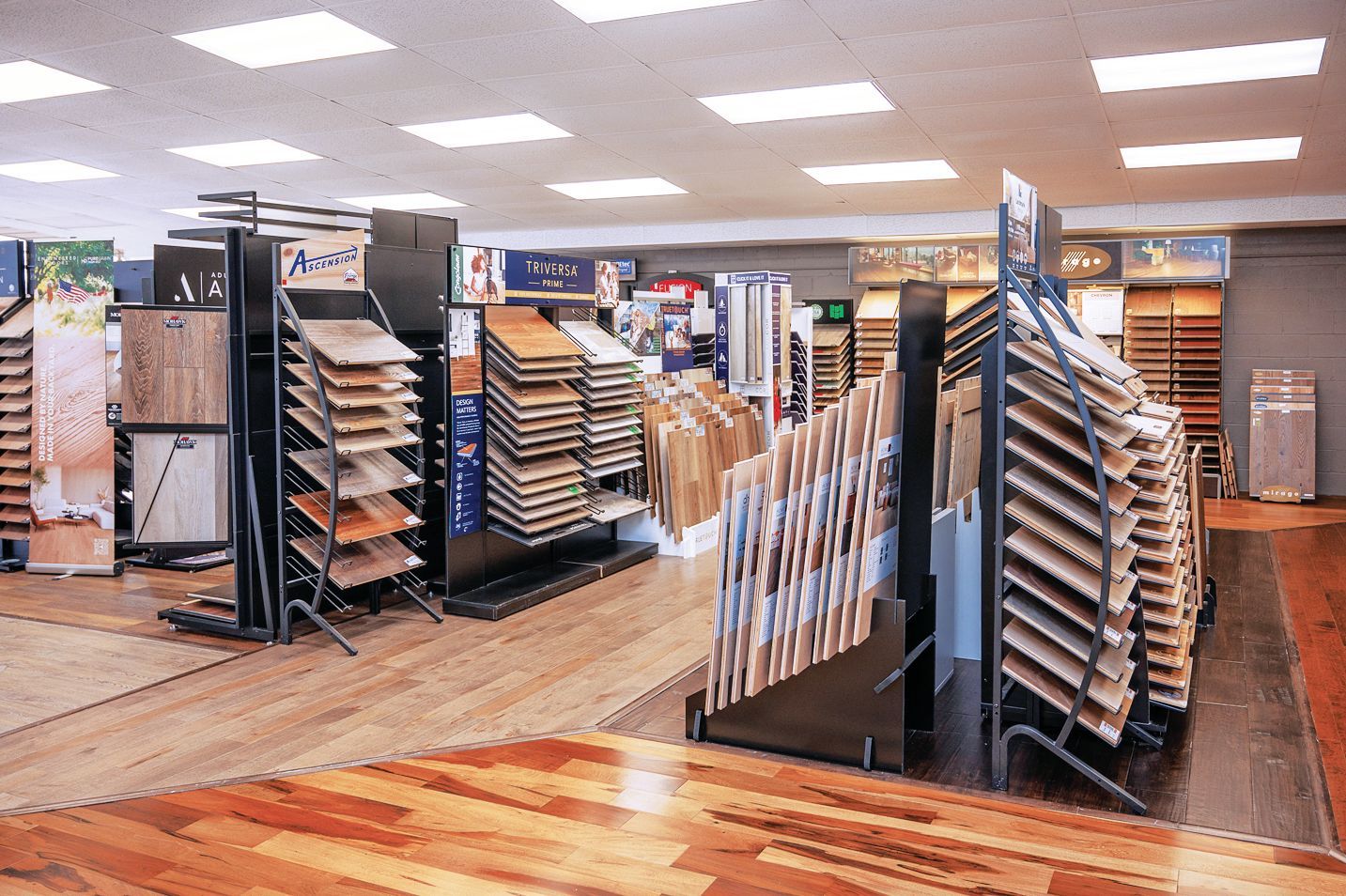 A flooring showroom featuring numerous display racks filled with various wood, tile, and laminate flooring samples.