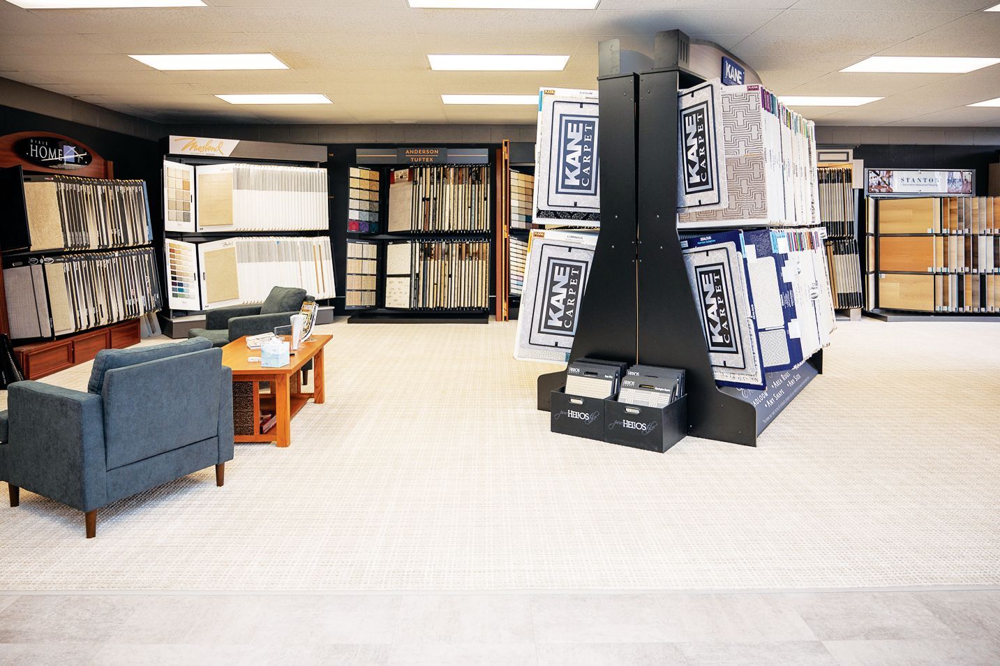 A carpet and flooring showroom displays organized product samples, a customer seating area, and shelves of flooring tiles.