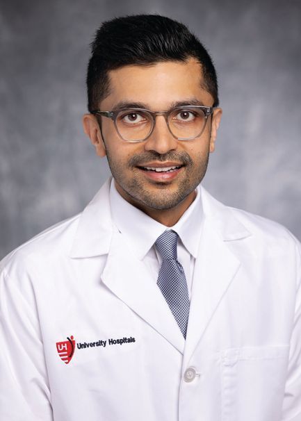 A professional headshot of a person in a white medical lab coat with a stethoscope and University Hospitals logo.