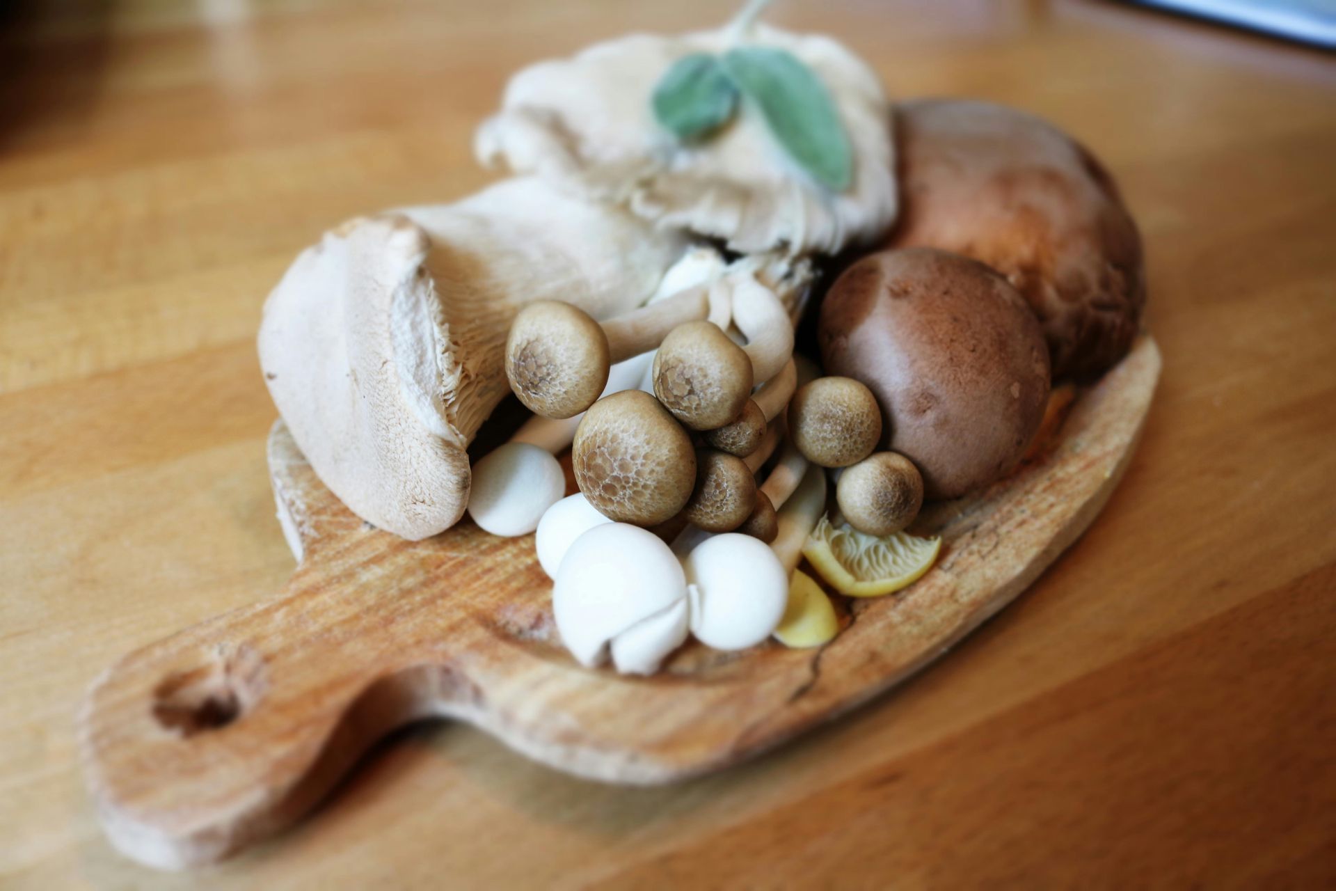 A variety of mushrooms including brown cremini and small clustered shimeji arranged on a wooden cutting board.