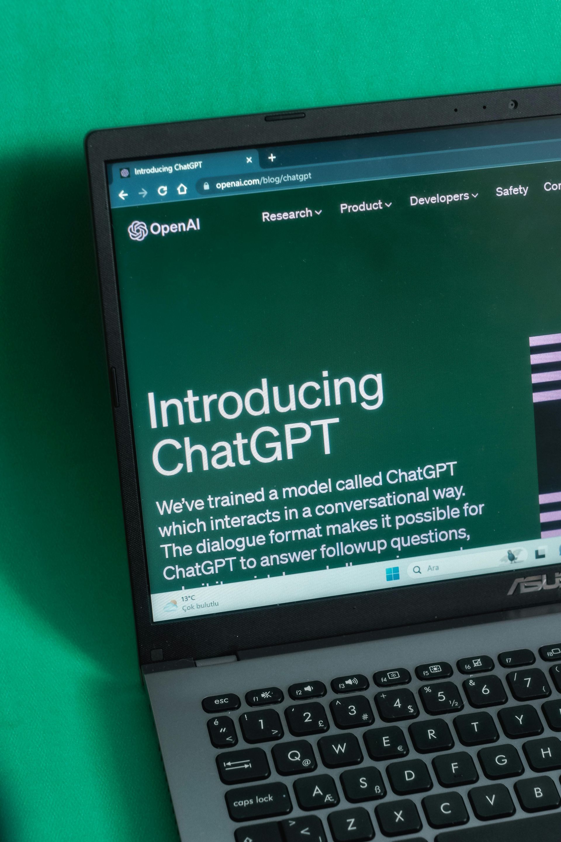 An ASUS laptop screen displaying the OpenAI webpage announcing the introduction of ChatGPT on a green background.