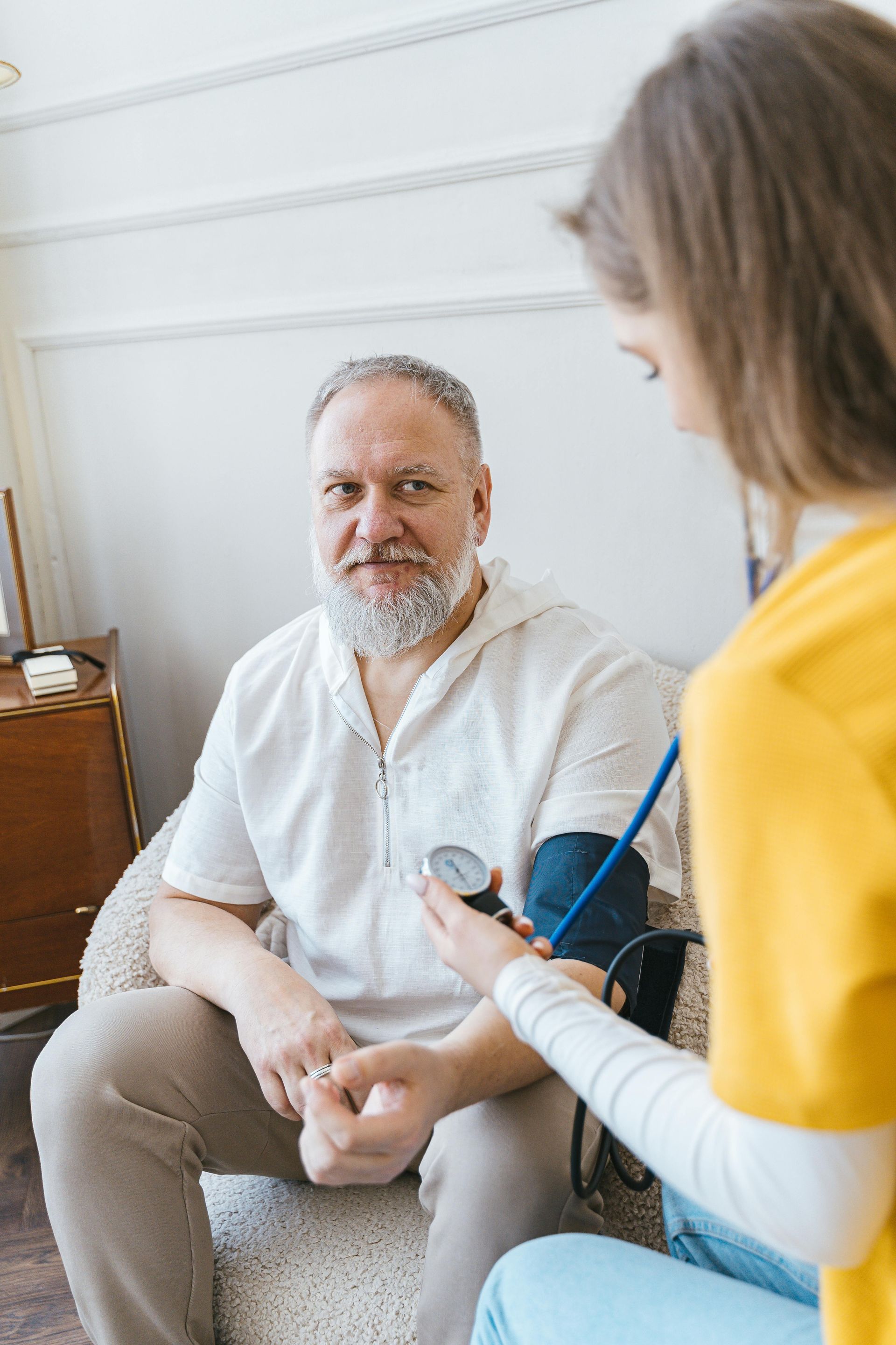 A healthcare professional in yellow scrubs uses a blood pressure cuff on a patient seated in a bright room.