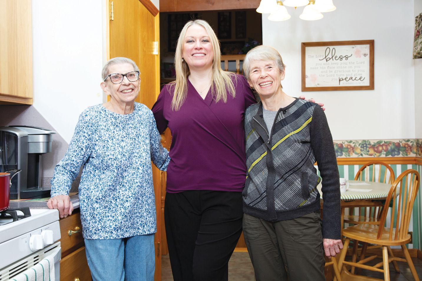 Three smiling people stand side-by-side in a kitchen, posing for a photo.
