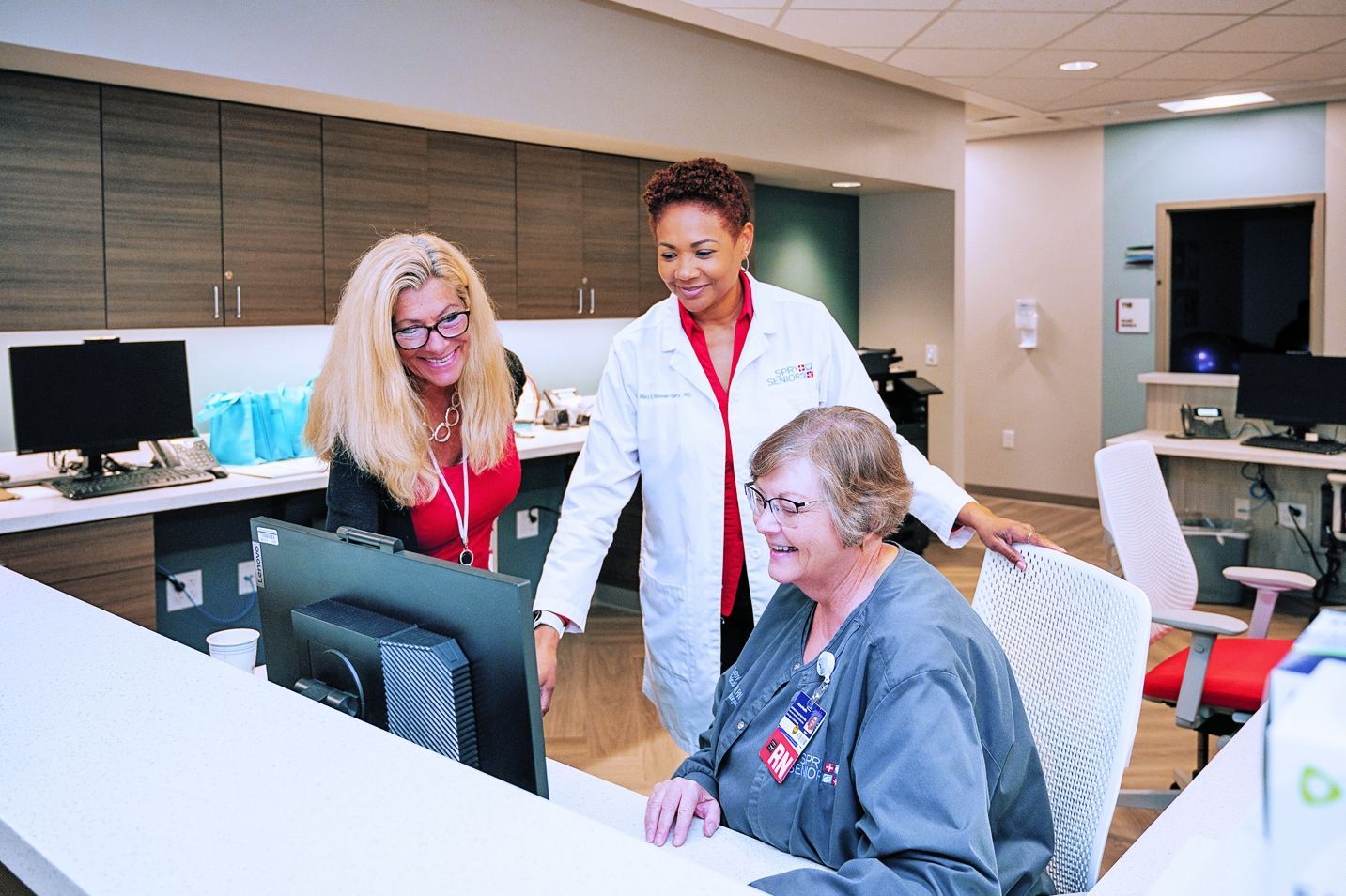 Three healthcare professionals in a clinic workspace collaborate while looking at a computer screen.