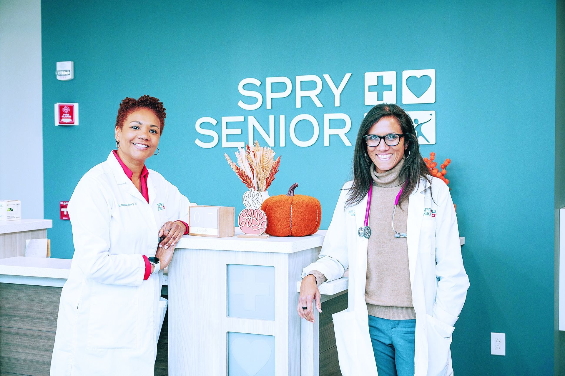 Two medical professionals in white coats stand in front of a teal 