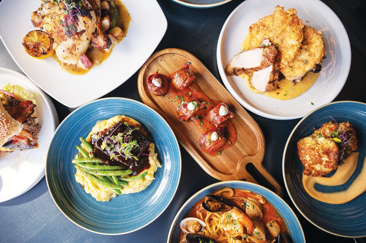 An overhead view of a table spread with various gourmet dishes, including roasted meats, pasta, and seafood.