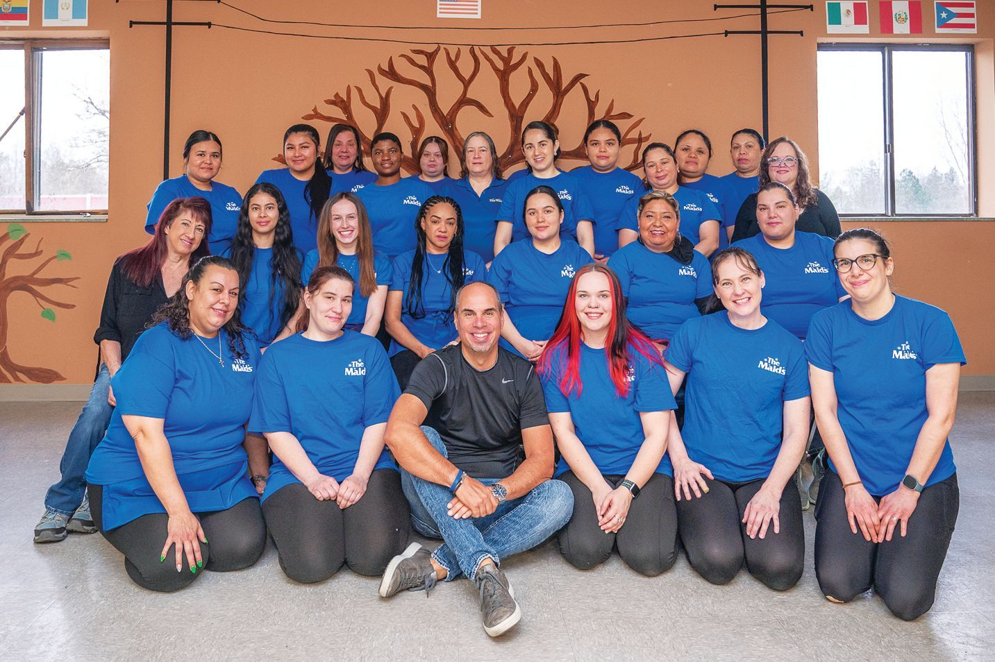 A group of people wearing blue shirts posing for a photo in front of a wall mural in a bright room.