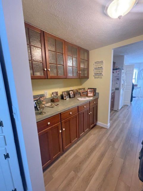 A buffet cabinet with wood cabinets, glass-front upper cupboards, and a countertop holding framed photos in a hallway.