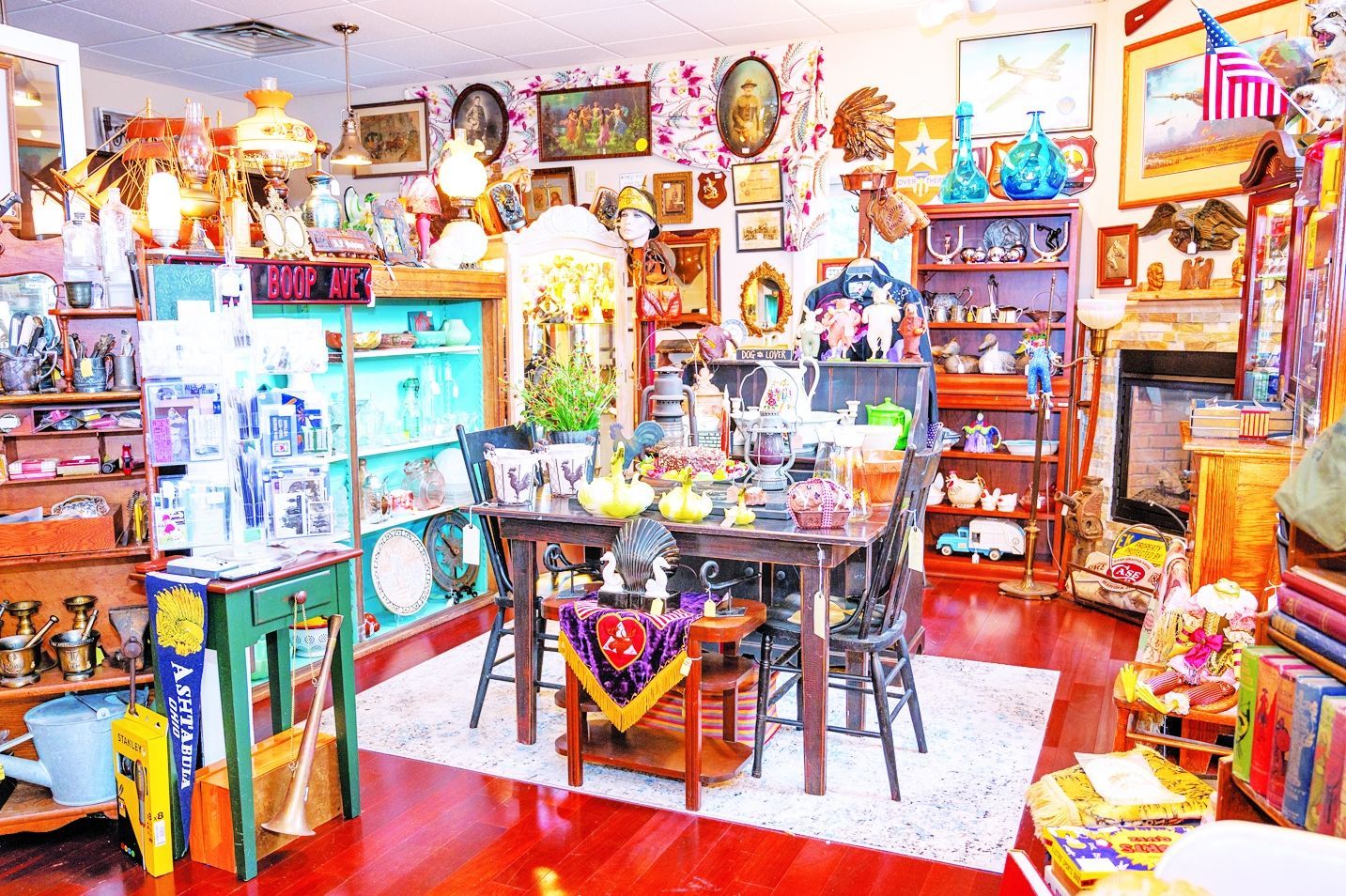 A cluttered antique shop with a wooden dining table, shelves filled with decor, and numerous wall hangings on red floors.