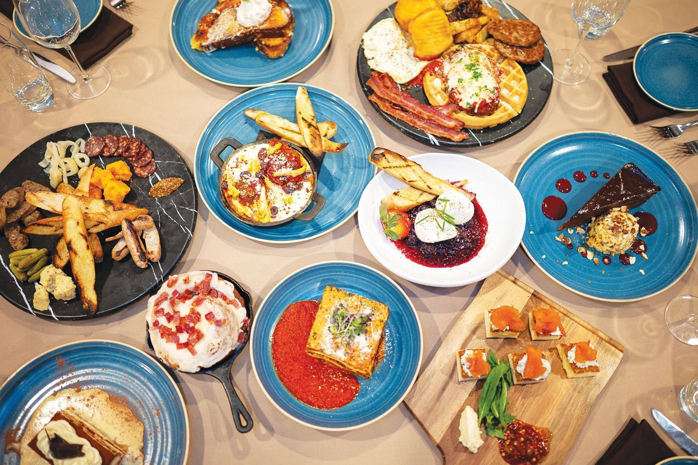 A flat-lay view of a wooden table covered with a variety of colorful brunch dishes served on vibrant blue and white plates.