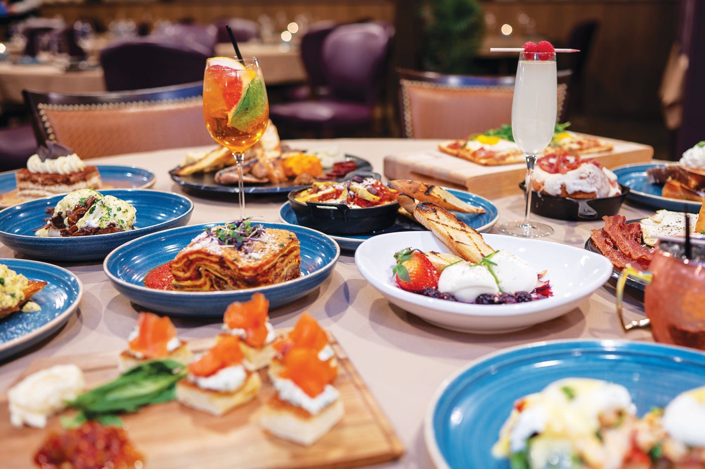 A table filled with a variety of gourmet brunch dishes, appetizers, and cocktails in a restaurant setting.