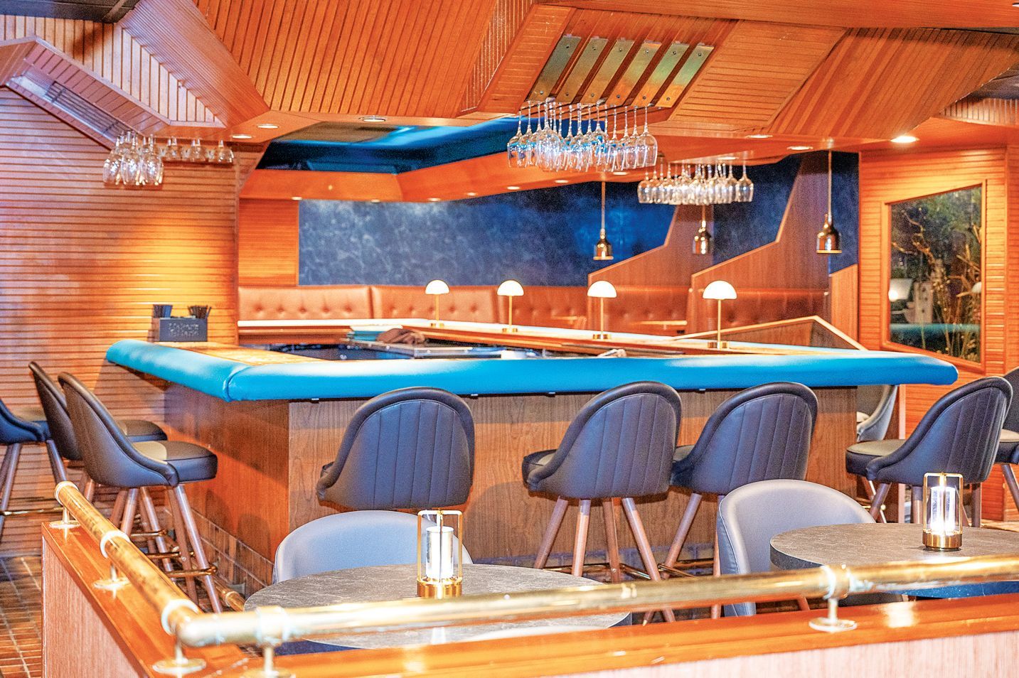 A bar with a blue countertop, dark chairs, and wood-paneled walls and ceiling in a dimly lit, upscale lounge.