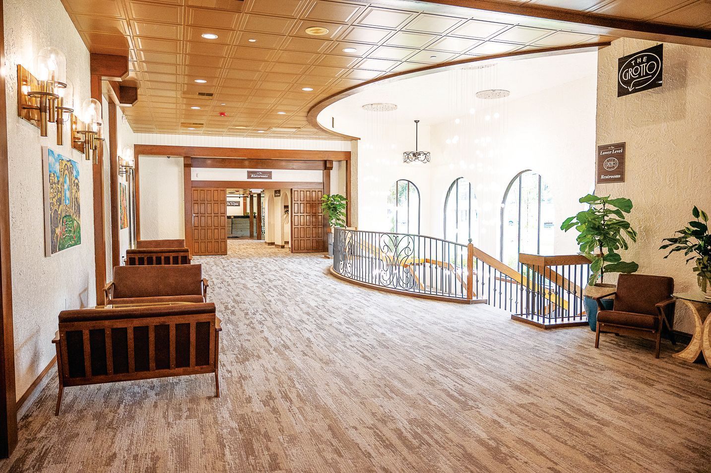 A lobby with carpeted floors, wooden furniture, and a decorative ceiling overlooking an open stairwell.