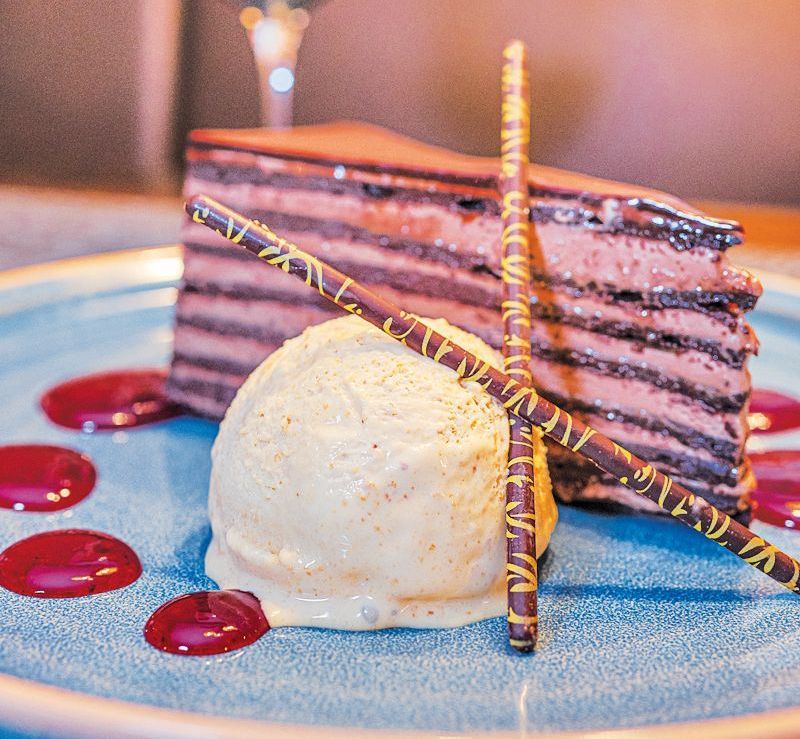 A slice of layered chocolate cake with a scoop of vanilla ice cream, topped with chocolate sticks on a blue plate.