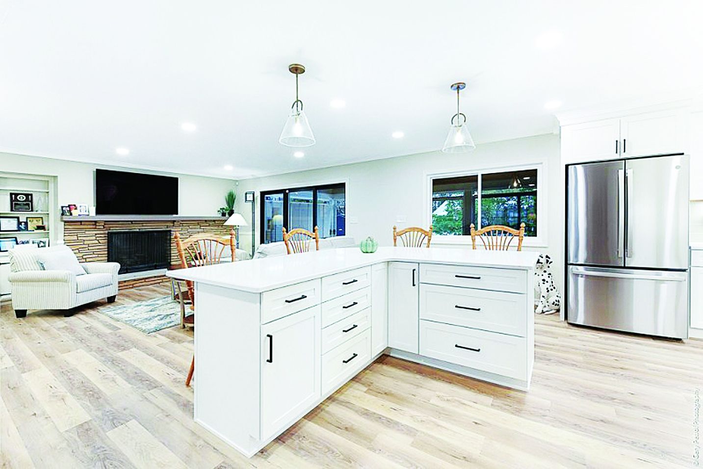 A modern open-plan kitchen with white cabinetry, a large central island, stainless steel refrigerator, and living area.