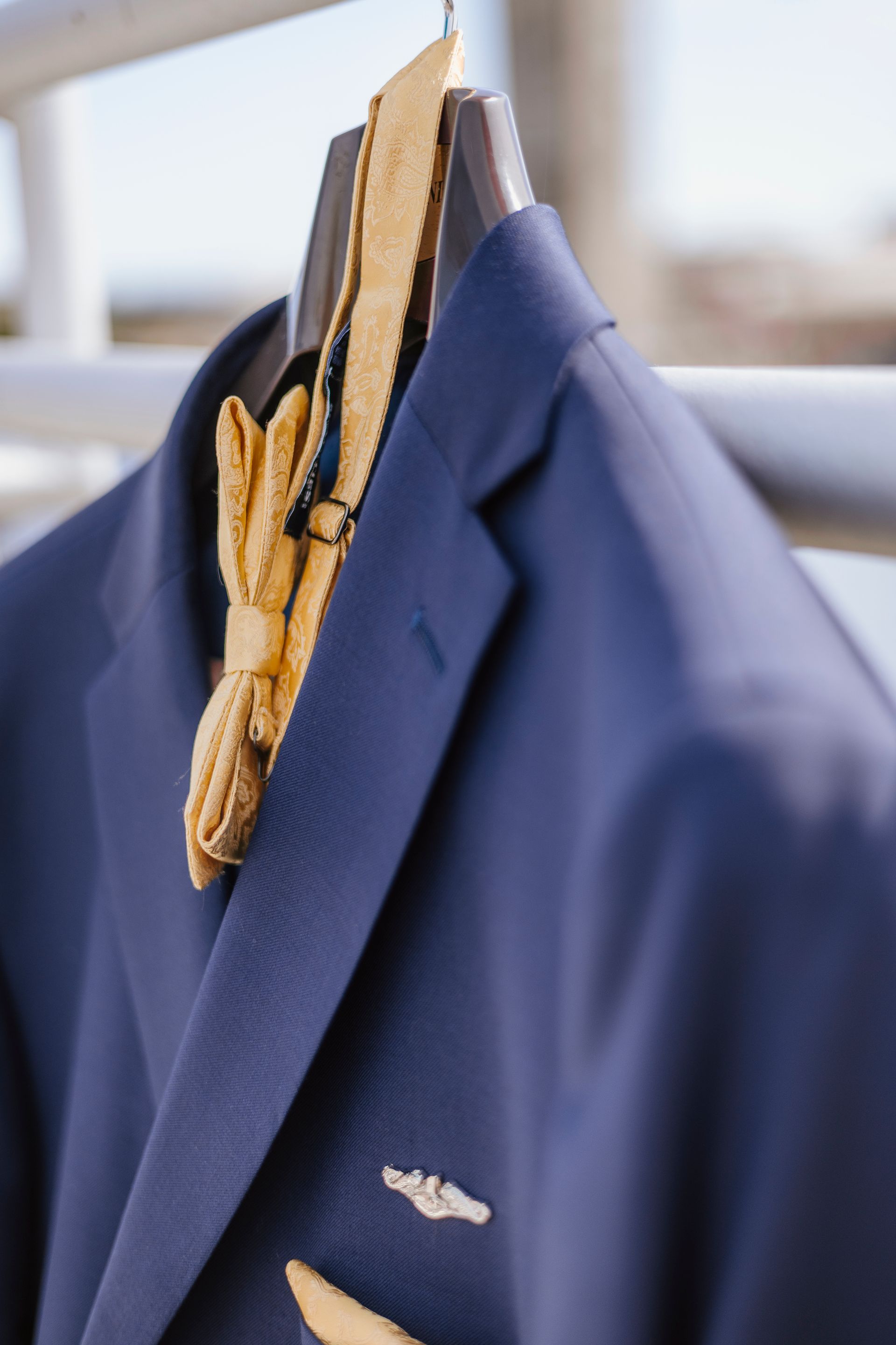 A blue suit with a yellow bow tie is hanging on a hanger.