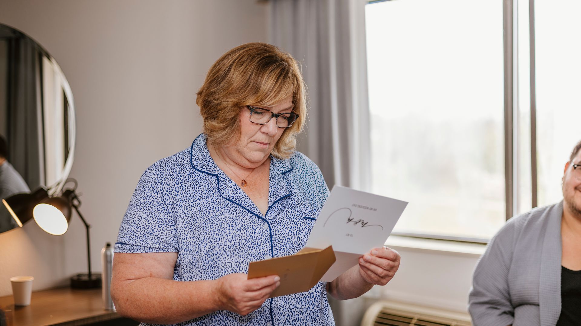 A woman is reading a letter in a hotel room.
