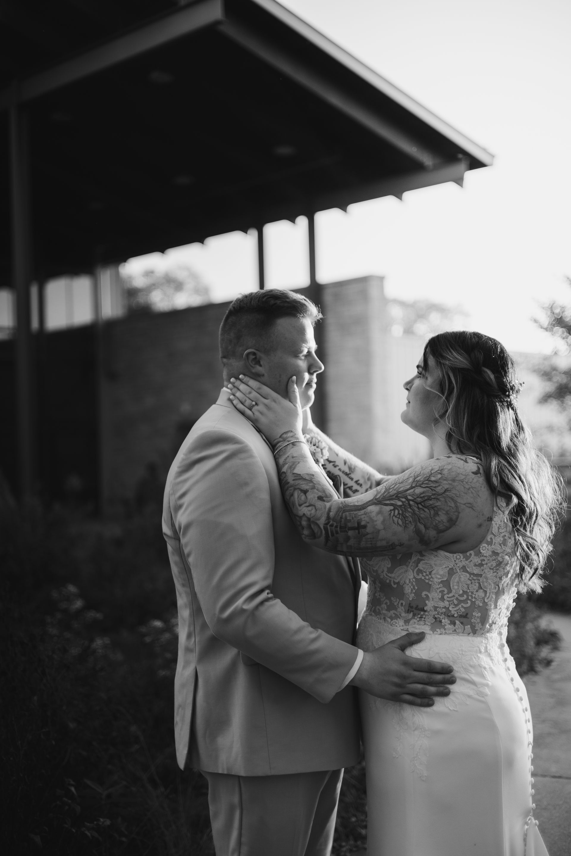 Couple embracing outdoors under a covered patio, with the bride touching the groom’s face.