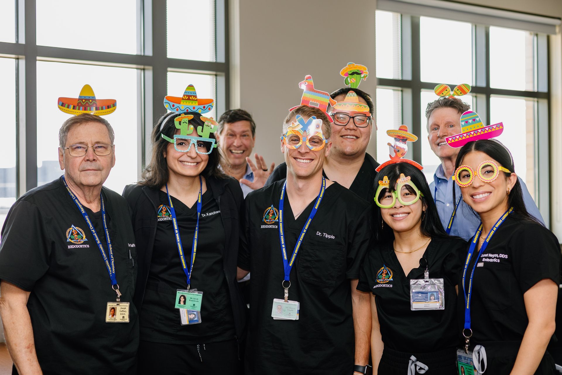 Smiling team in black shirts wearing colorful decorative headbands, standing in front of windows and posing together