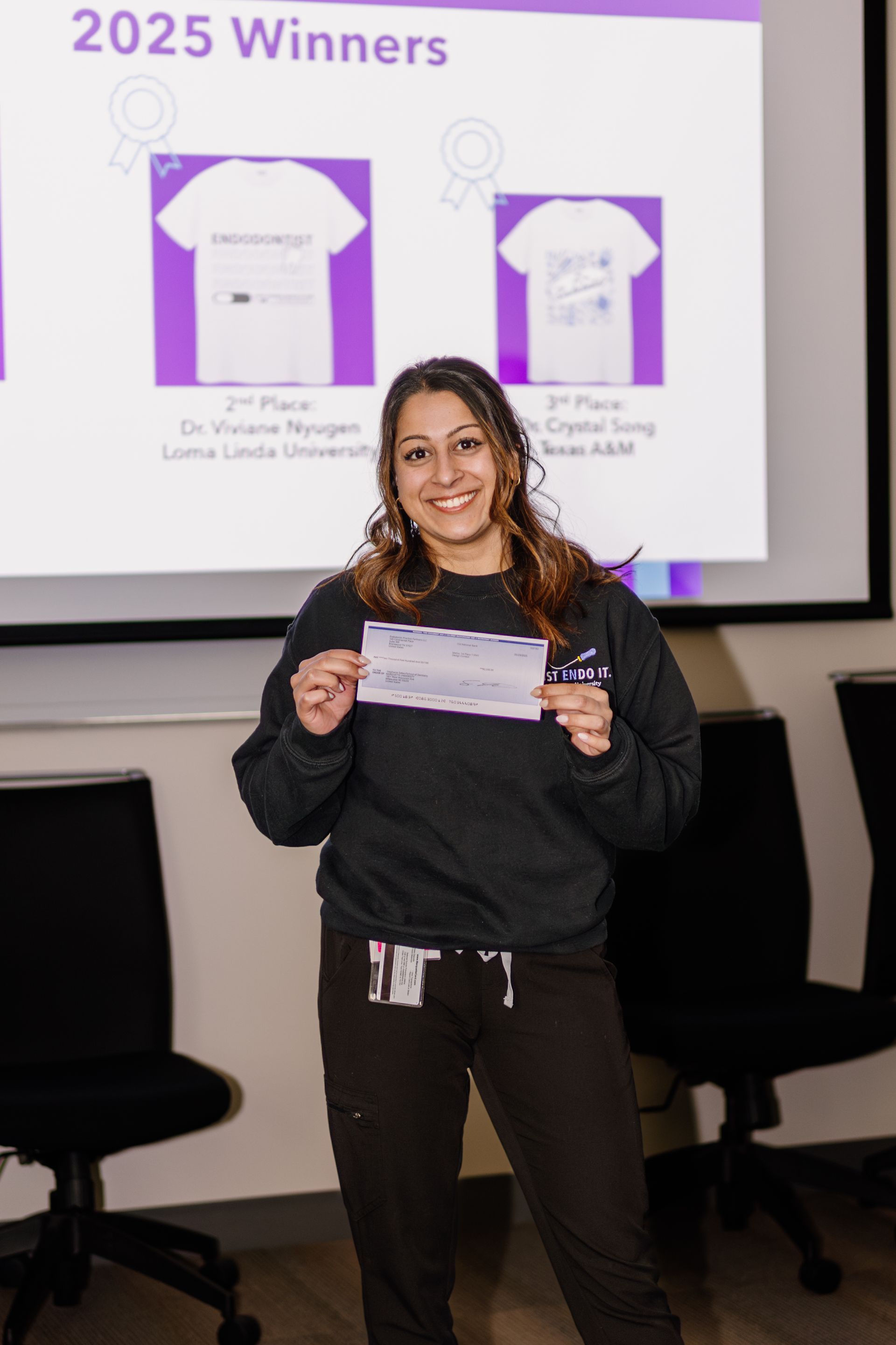 Woman holding a certificate in front of a “2025 Winners” presentation screen.