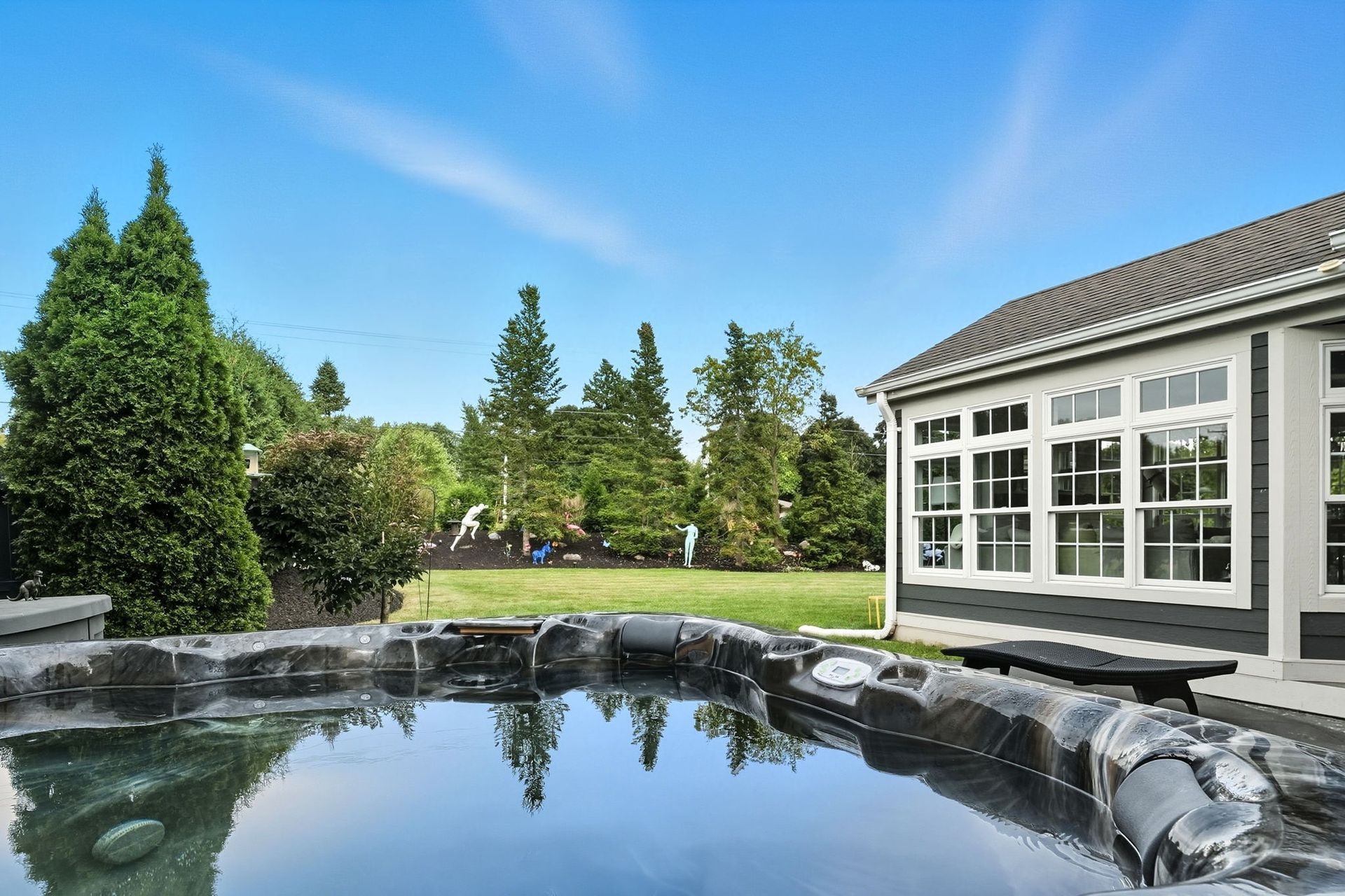 Backyard pond beside a house, with trees and a clear blue sky