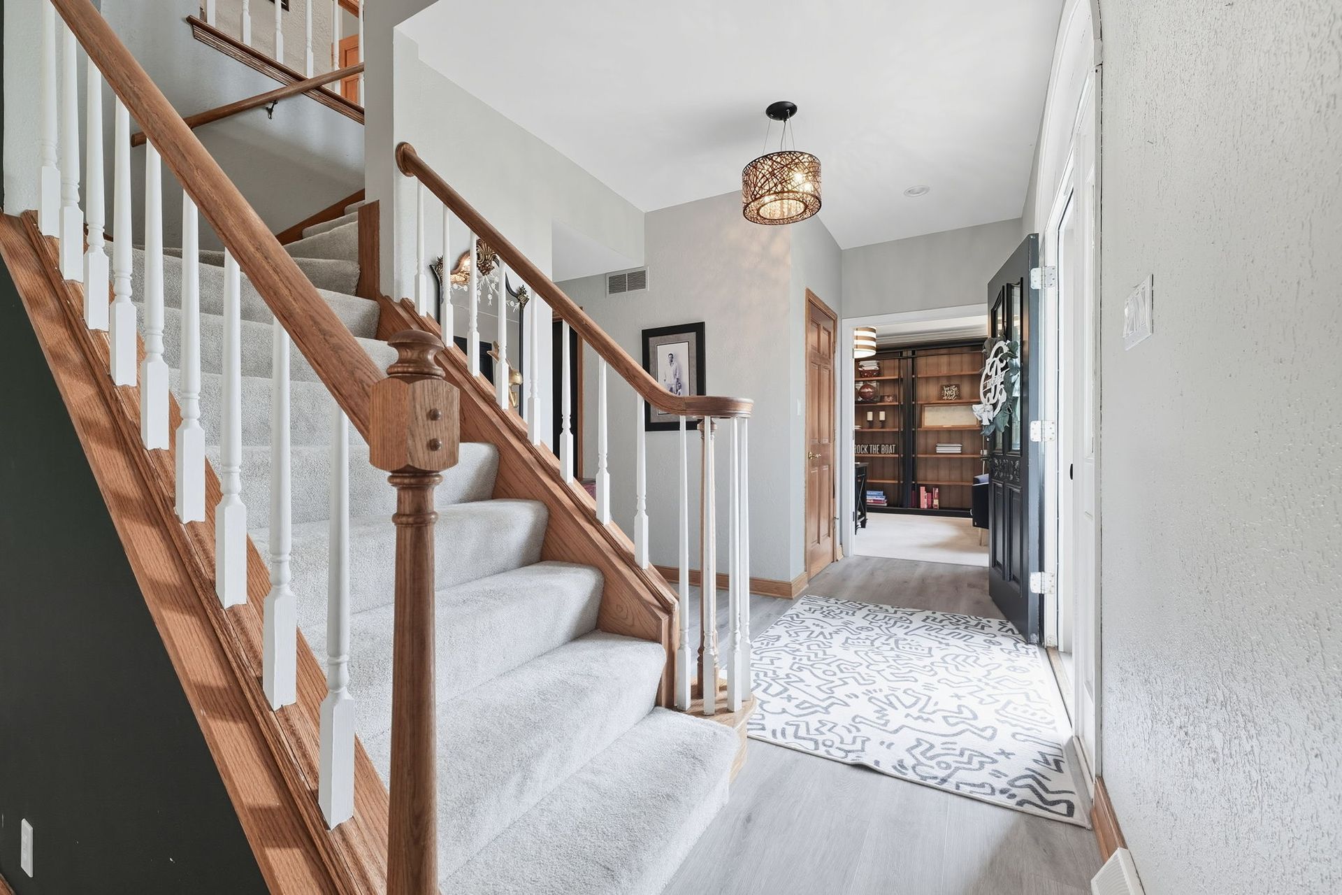 Carpeted staircase with wooden railing leading to a bright hallway and front door.
