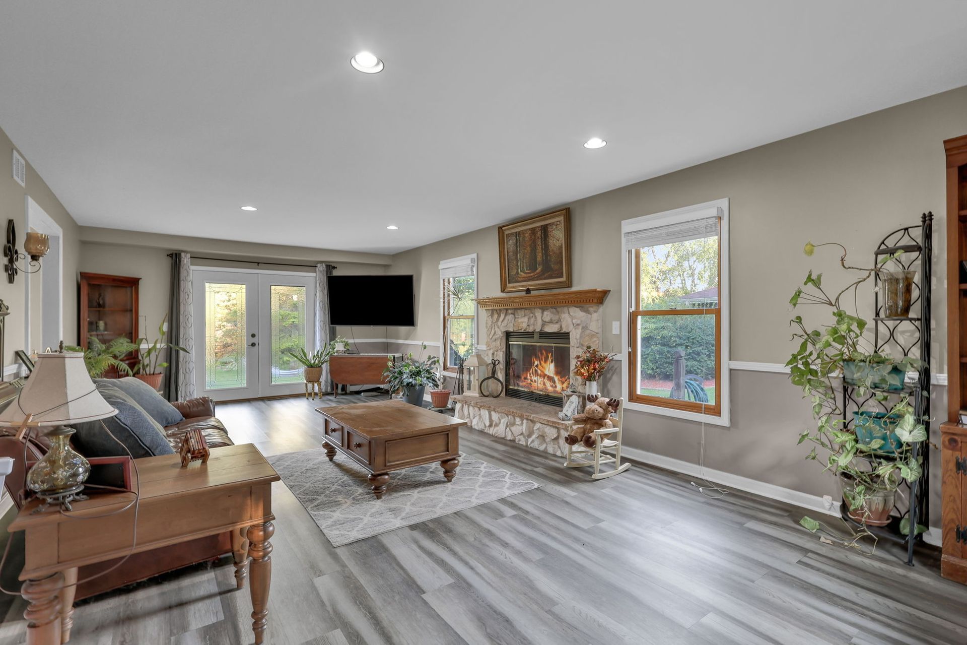 Bright living room with fireplace, TV, gray floors, and large windows opening to a patio