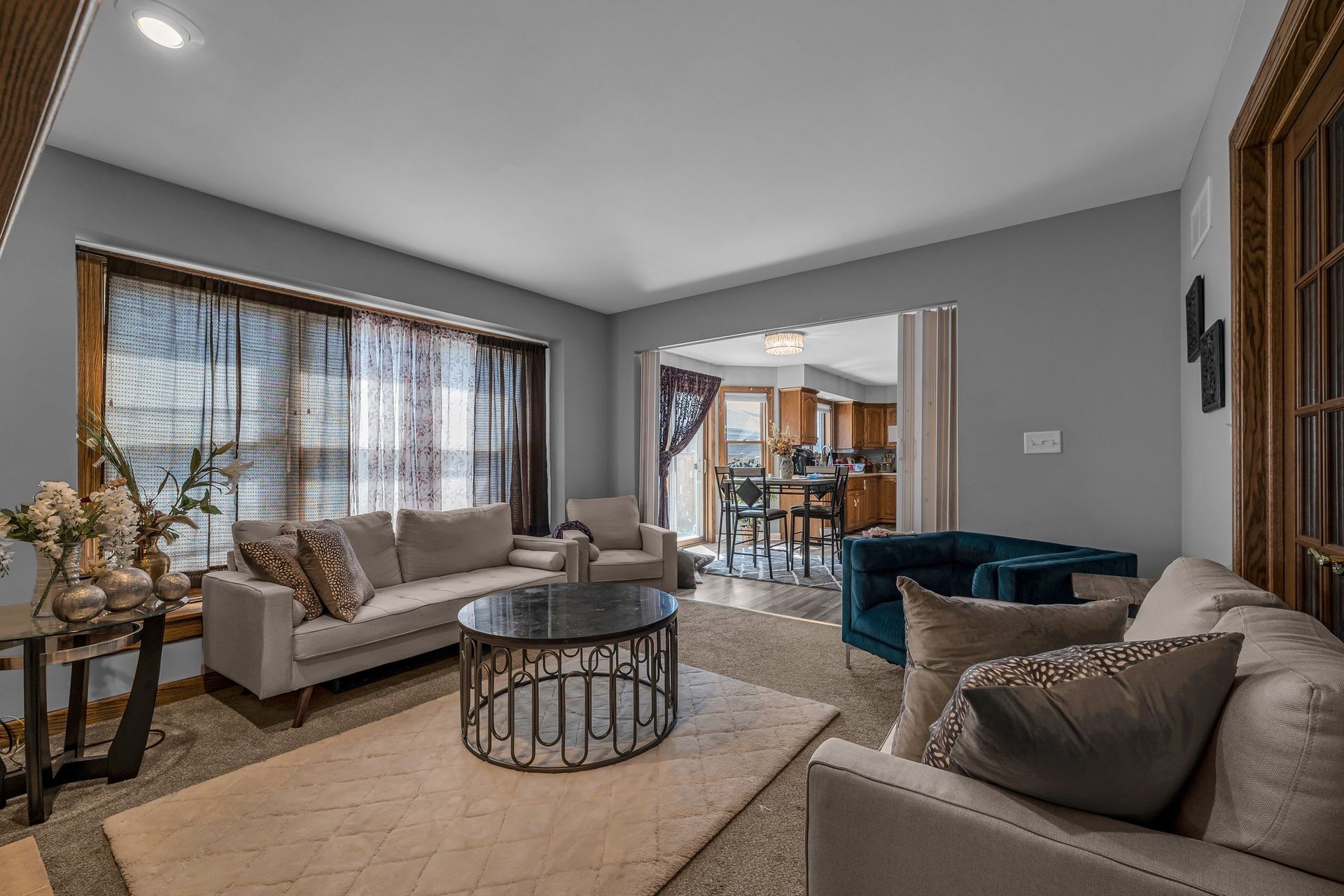 Modern living room with gray sofas, round coffee table, and large windows opening to a dining area.