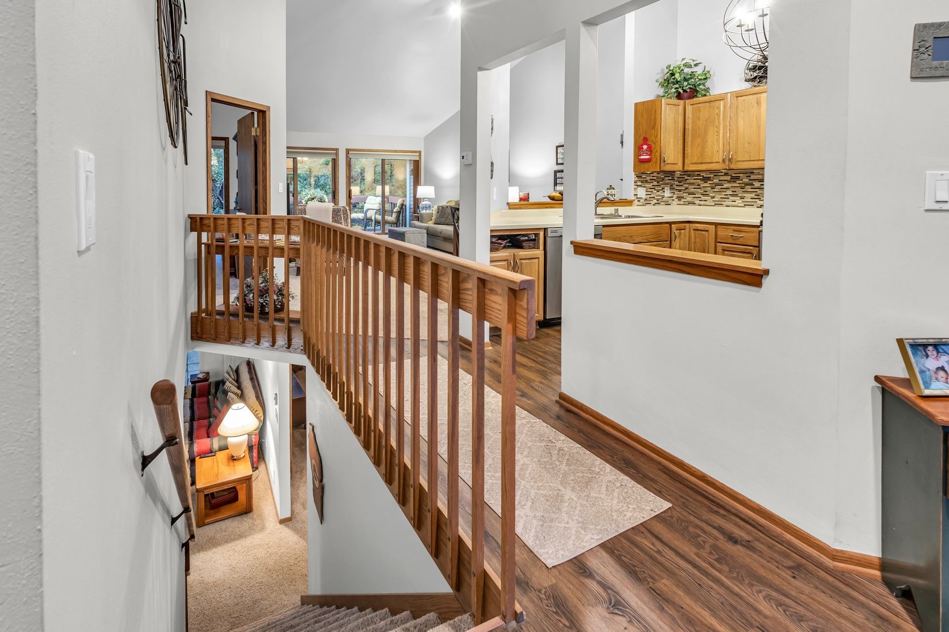 Stair landing with wooden railing overlooking a bright home interior and kitchen.