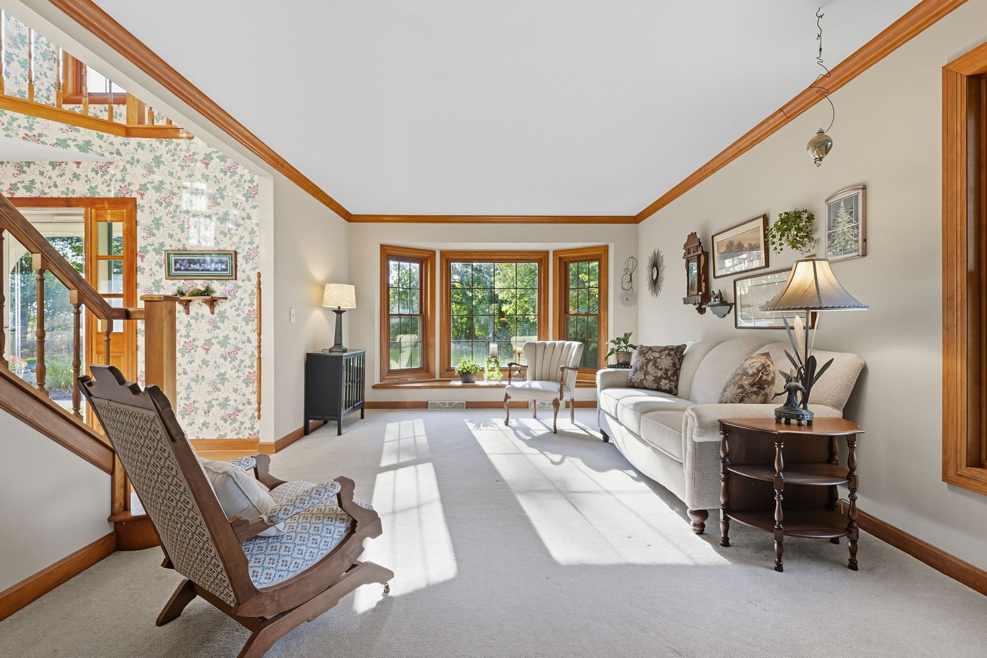 Bright living room with white walls, wood trim, gray sofa, rocking chair, and large sunny windows