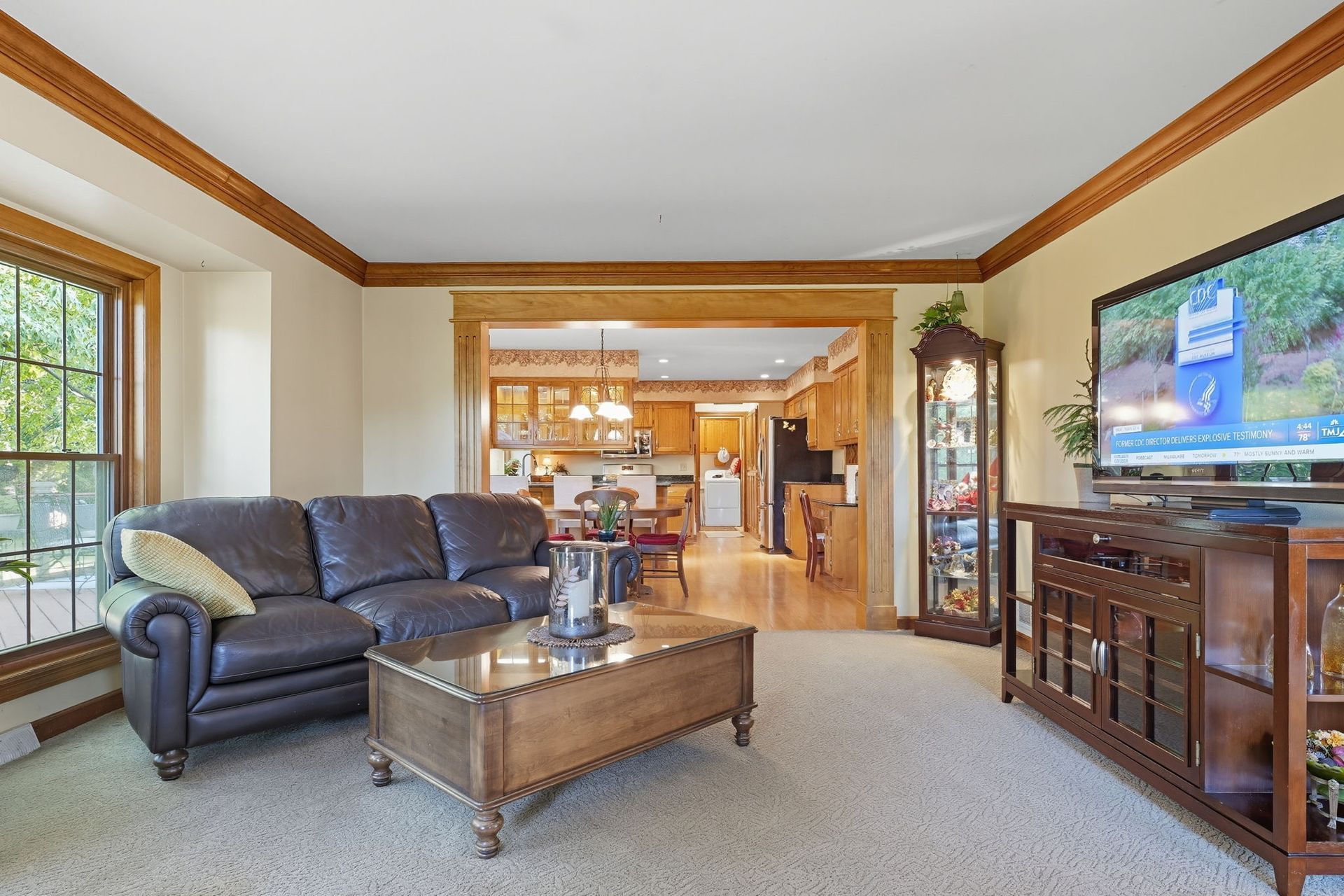 Bright living room with dark leather sofa, wooden coffee table, TV, and open view to a kitchen