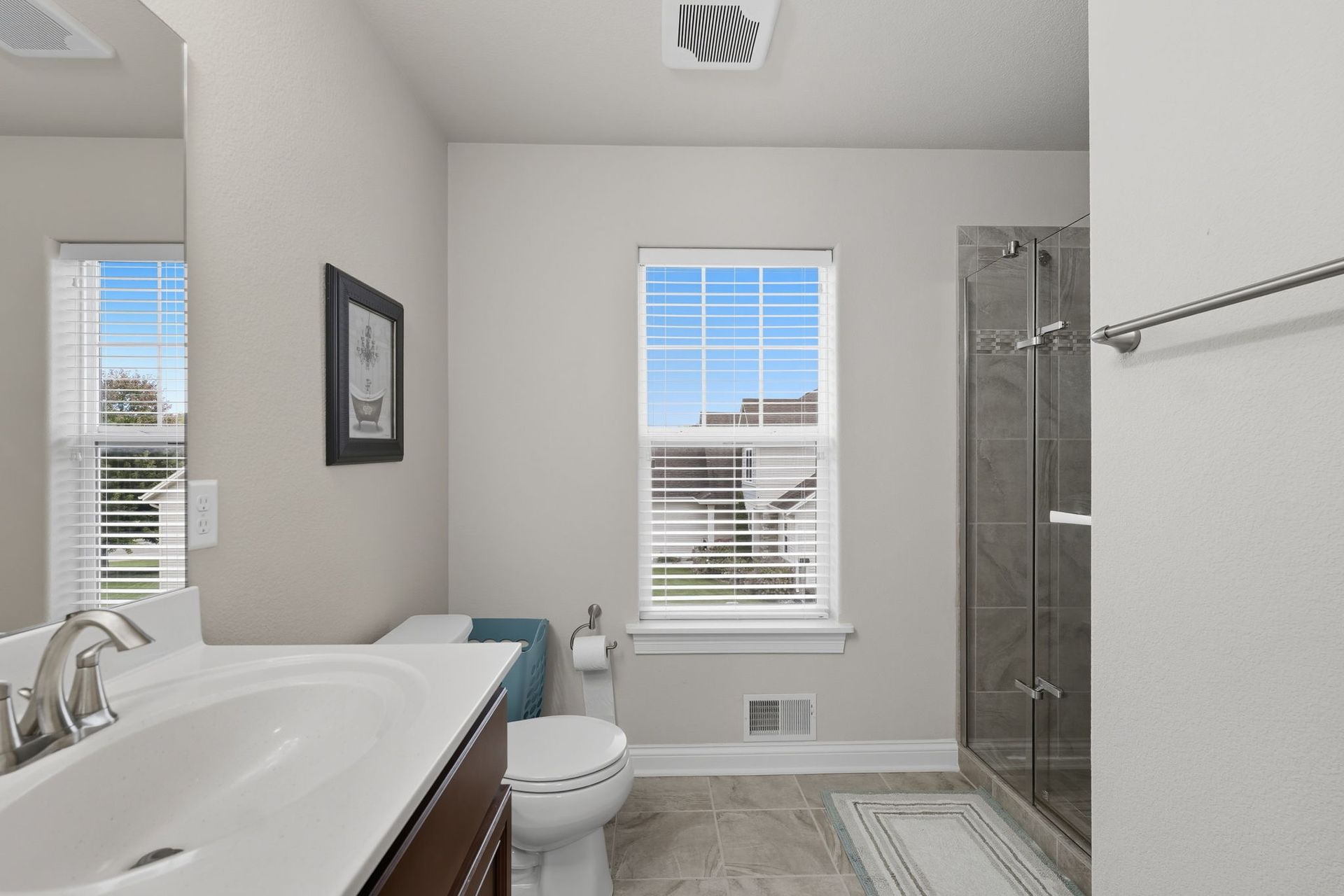 Bright bathroom with a bathtub, toilet, shower, and two windows letting in daylight.