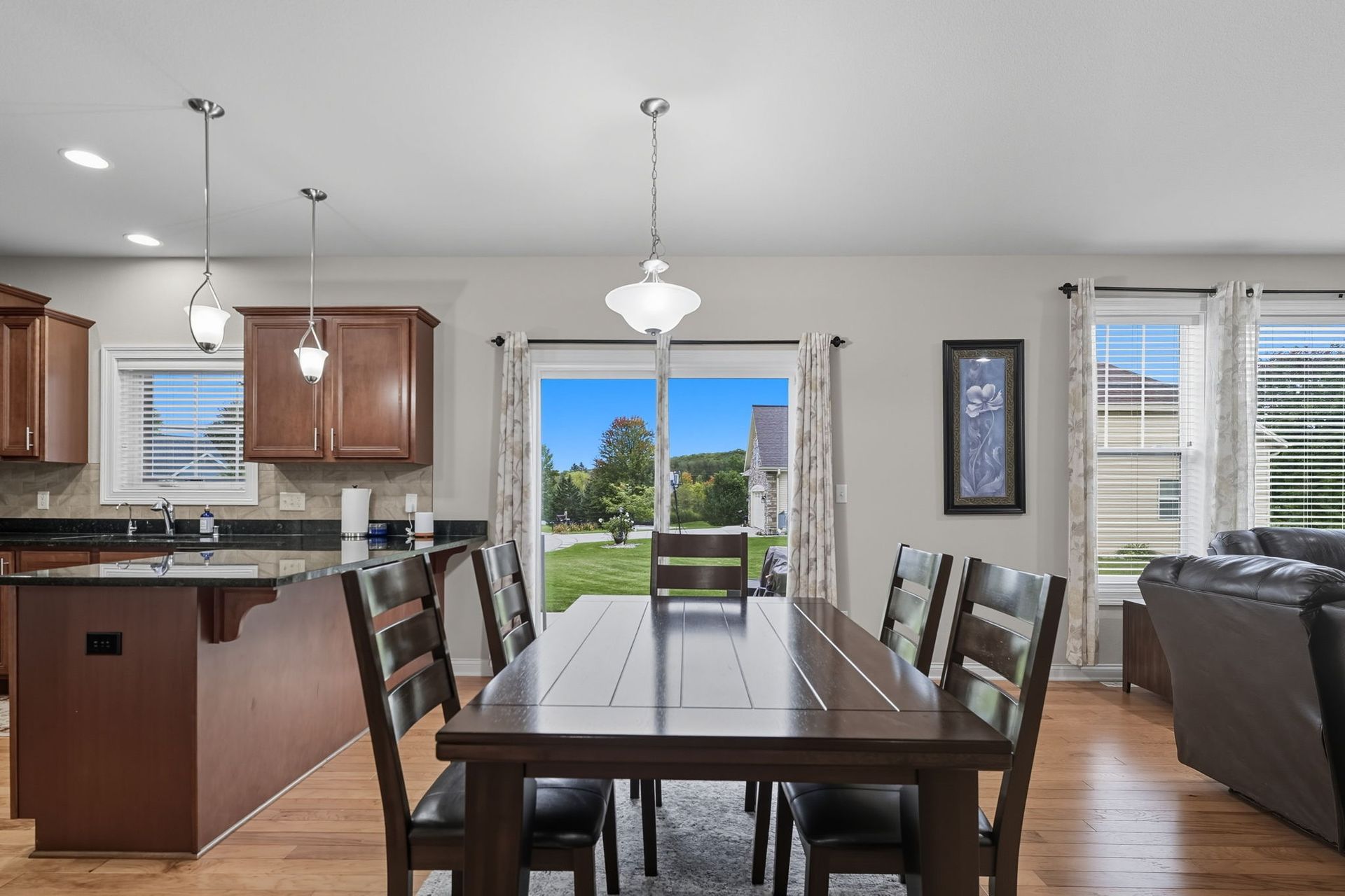 Open-concept dining room with a dark wood table, kitchen, and sliding glass doors to a patio and backyard.