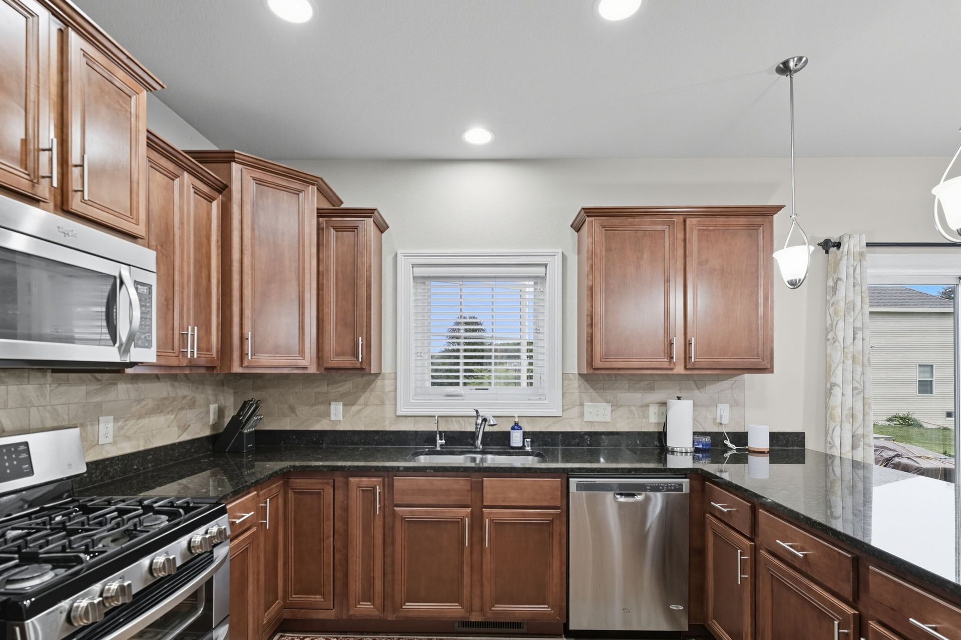 Modern kitchen with wood cabinets, stainless appliances, black countertops, and a window over the sink
