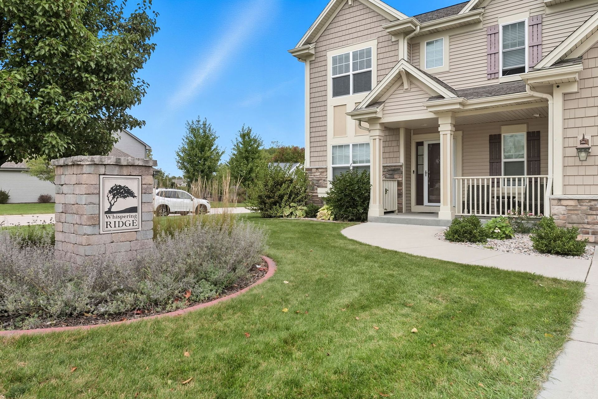 Suburban house entrance with manicured lawn, porch, and stone neighborhood sign